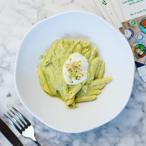 Green Table Cafe's penne pasta with creamy pesto sauce, topped with a dollop of white cream and sprouts.