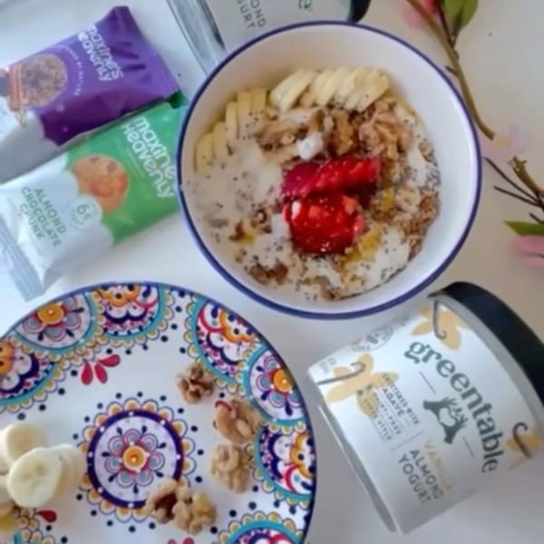 Overhead view of a Green Table Cafe yogurt bowl with fruit, nuts, and granola, alongside snacks.