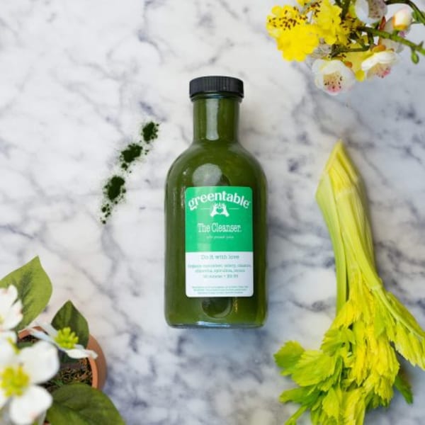 Green Table Cafe's "The Cleanser" juice bottle on marble, with celery and flowers.