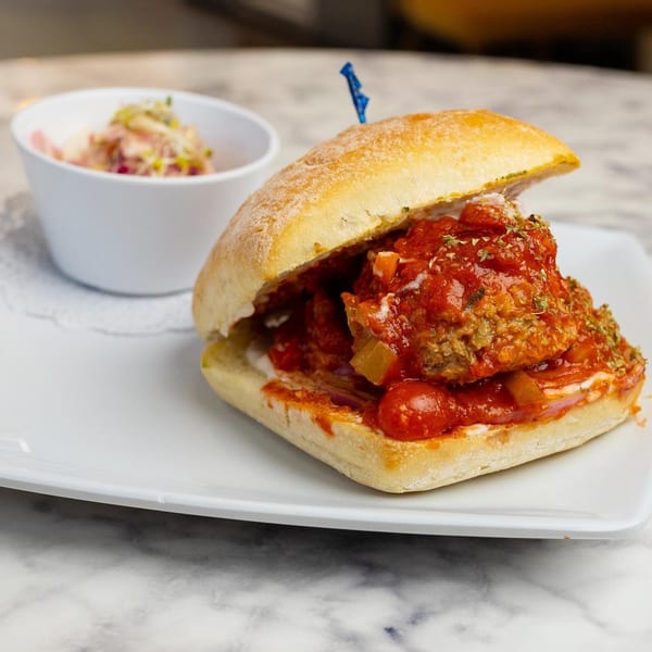 Meatball sub sandwich with red sauce and herbs, served with a side of coleslaw.