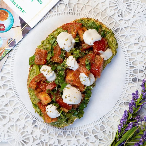 Avocado toast with diced tomatoes, mozzarella, and herbs on a white lace placemat.