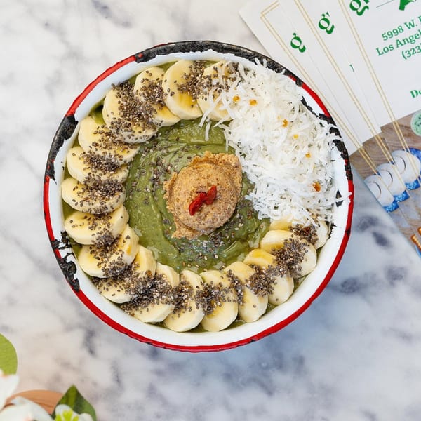 A vibrant green smoothie bowl topped with banana slices, chia seeds, shredded coconut, and nut butter.