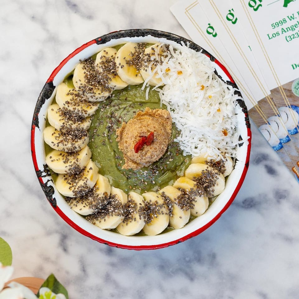 A vibrant green smoothie bowl topped with banana slices, chia seeds, shredded coconut, and nut butter.