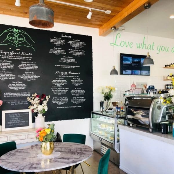 Interior of Green Table Cafe with a large chalkboard menu, marble table, and coffee bar.