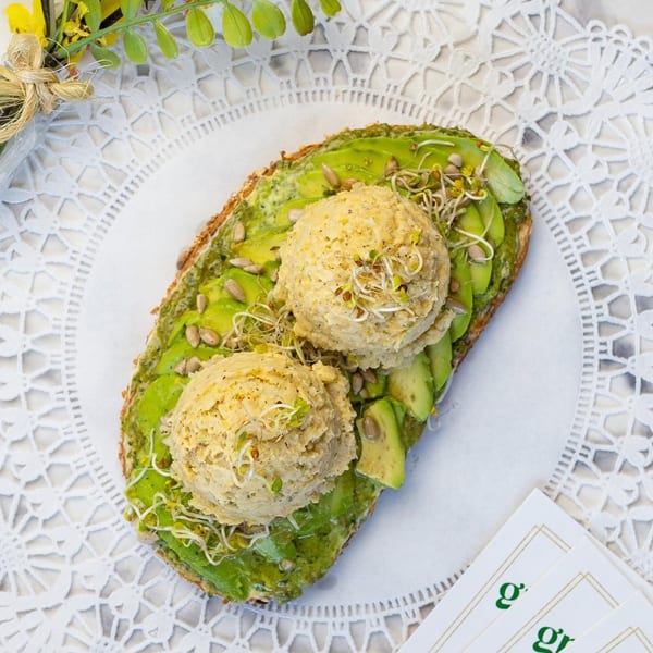 Avocado toast with two scoops of chickpea salad, sunflower seeds, and sprouts on a white doily.