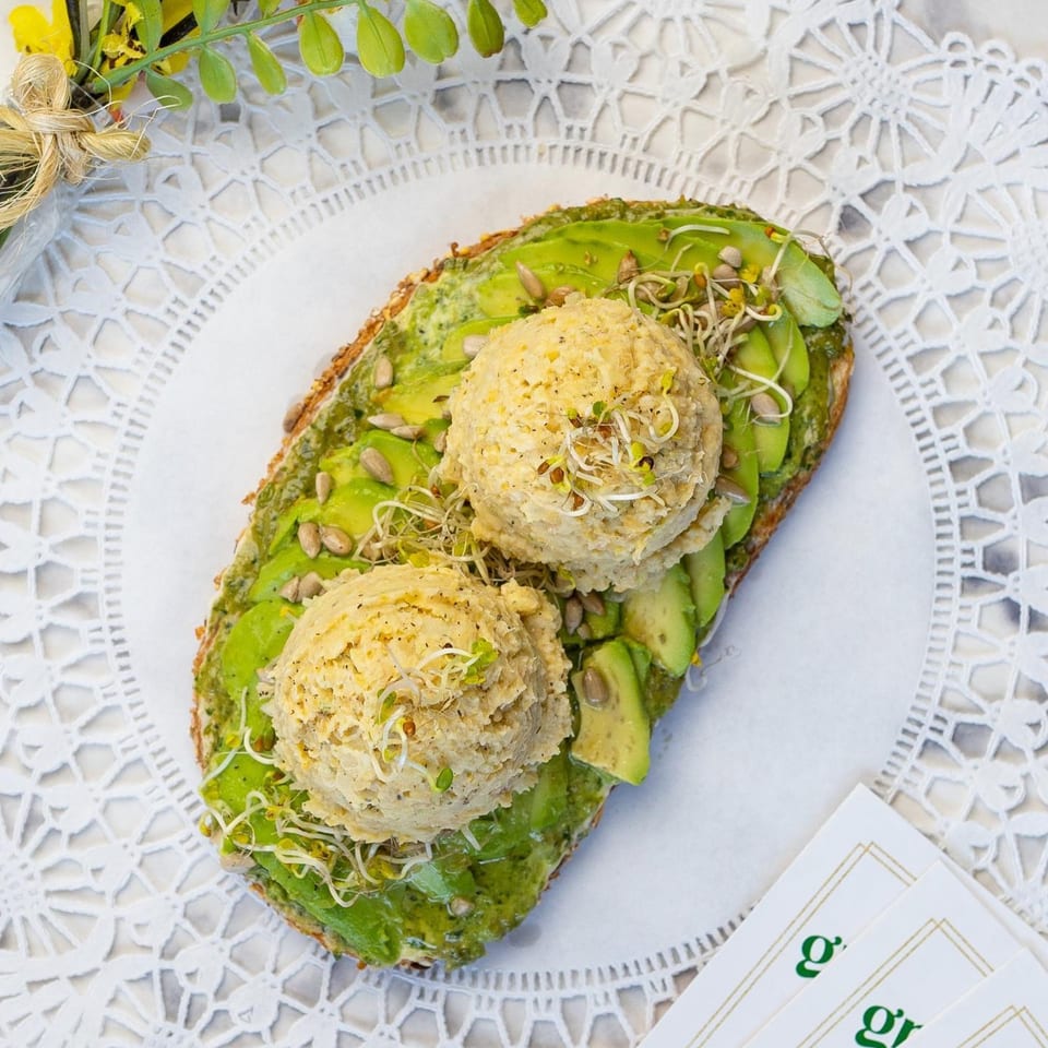 Avocado toast with two scoops of chickpea salad, sunflower seeds, and sprouts on a white doily.