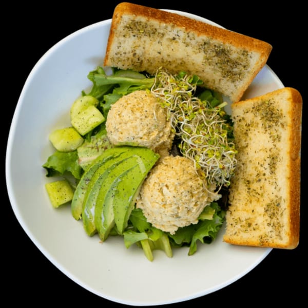 Green Table Cafe's salad with tuna scoops, avocado, sprouts, and garlic bread on a white plate.