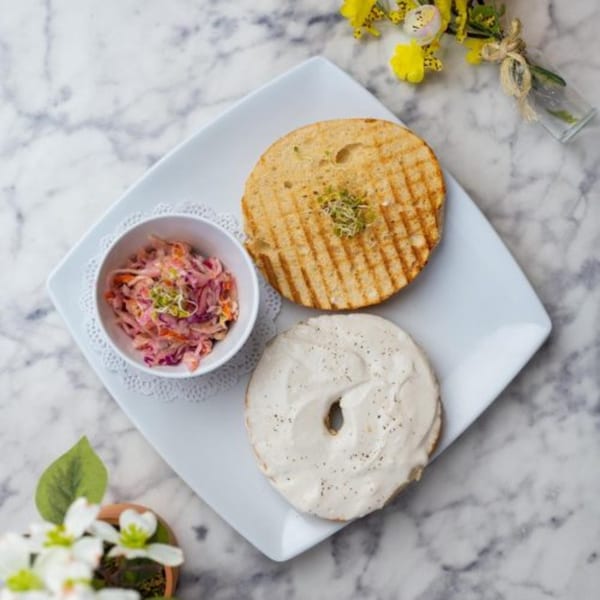 Toasted bagel half with sprouts, bagel with cream cheese, and a side of coleslaw on a white plate.