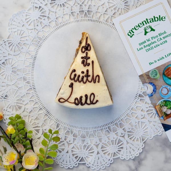 A slice of cake with "Do it with Love" written in chocolate, next to a Green Table Cafe card.