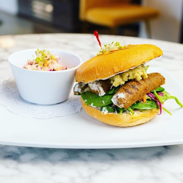 A vegan sausage sandwich with greens and sauce, served with a side of coleslaw.