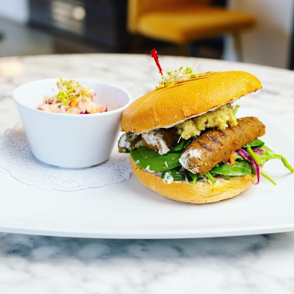 A vegan sausage sandwich with greens and sauce, served with a side of coleslaw.