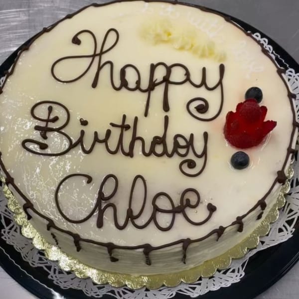 White frosted birthday cake with "Happy Birthday Chloe" in chocolate, topped with berries.