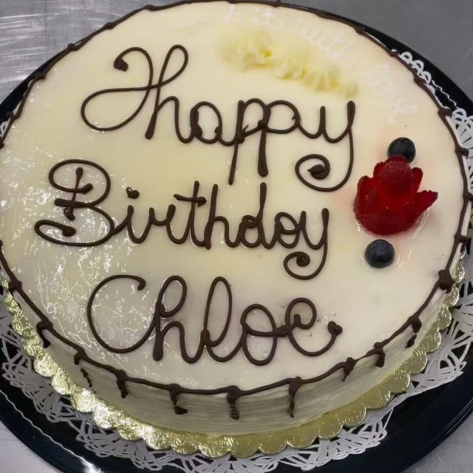 White frosted birthday cake with "Happy Birthday Chloe" in chocolate, topped with berries.