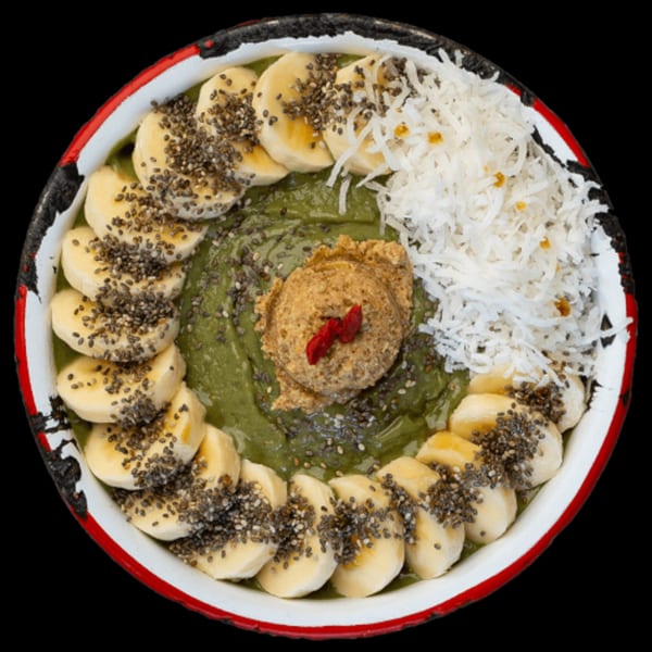 Green smoothie bowl topped with banana slices, chia seeds, shredded coconut, and a scoop of nut butter.