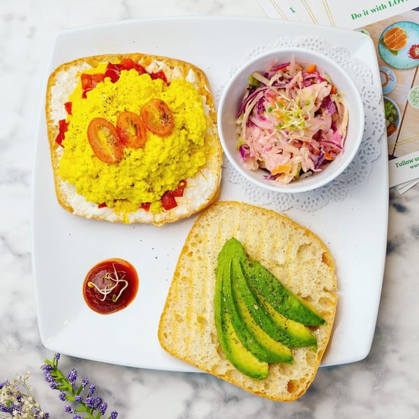 Scrambled eggs with tomatoes and red peppers, avocado toast, and coleslaw on a white plate.