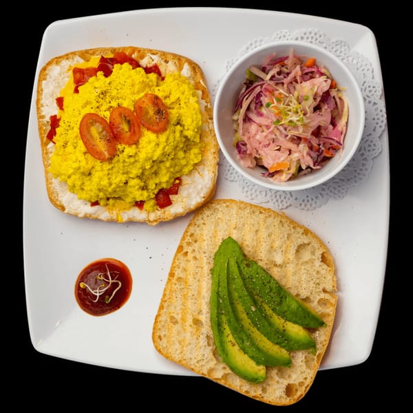 Scrambled tofu with tomatoes, avocado toast, and coleslaw on a white plate at Green Table Cafe.