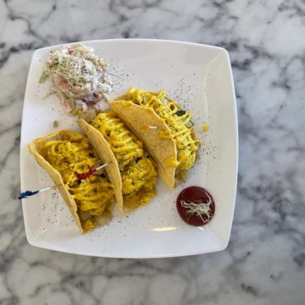 Three Green Table Cafe tacos filled with yellow scrambled eggs, served with coleslaw and ketchup.