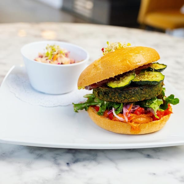 A Green Table Cafe veggie burger with zucchini and sprouts, served with a side of coleslaw.