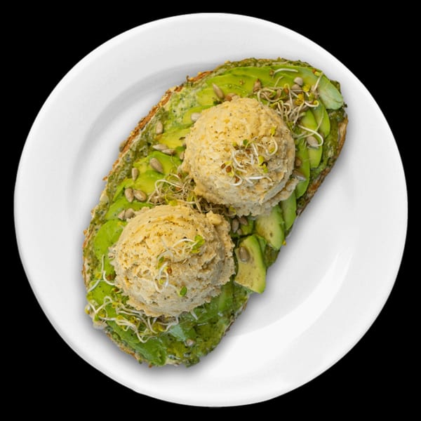 Avocado toast with two scoops of hummus, sunflower seeds, and sprouts on a white plate.