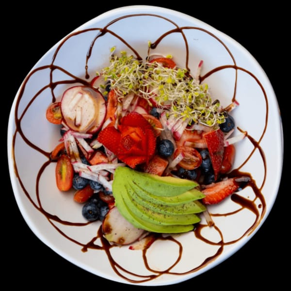 A vibrant Green Table Cafe salad with strawberries, blueberries, avocado, radishes, and sprouts, drizzled with balsamic glaze.