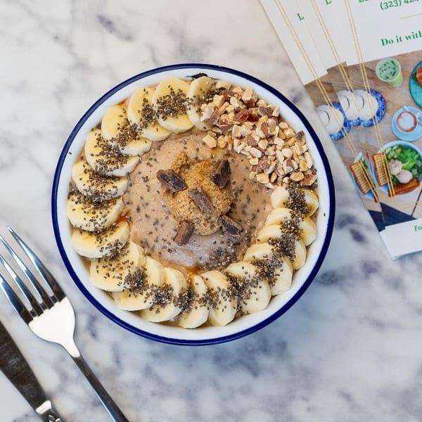 Overhead view of a Green Table Cafe smoothie bowl with bananas, nuts, chia seeds, and peanut butter.