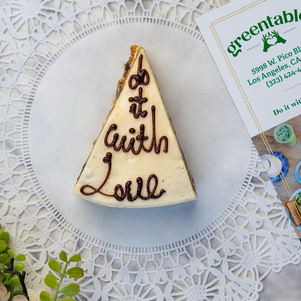 A slice of cake with "do it with Love" written in chocolate, next to a Green Table Cafe menu.