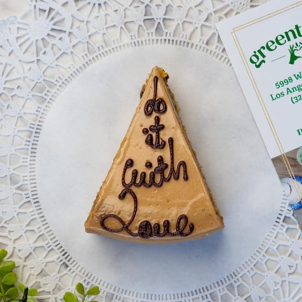 Slice of cake with "do it with Love" written in chocolate, next to a Green Table Cafe card.