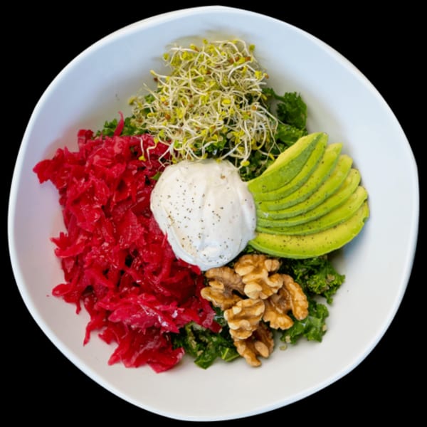 A vibrant Green Table Cafe bowl with red cabbage, avocado, sprouts, walnuts, and a dollop of cream.
