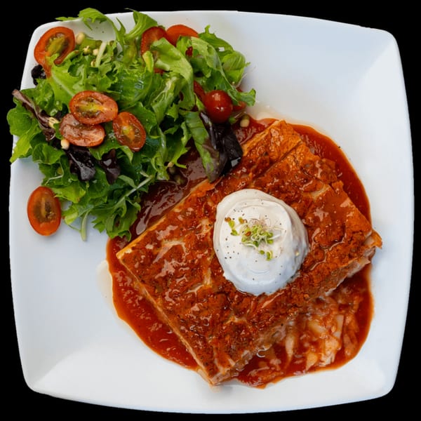 Green Table Cafe's lasagna with red sauce, topped with a dollop of cream and sprouts, alongside a fresh salad.