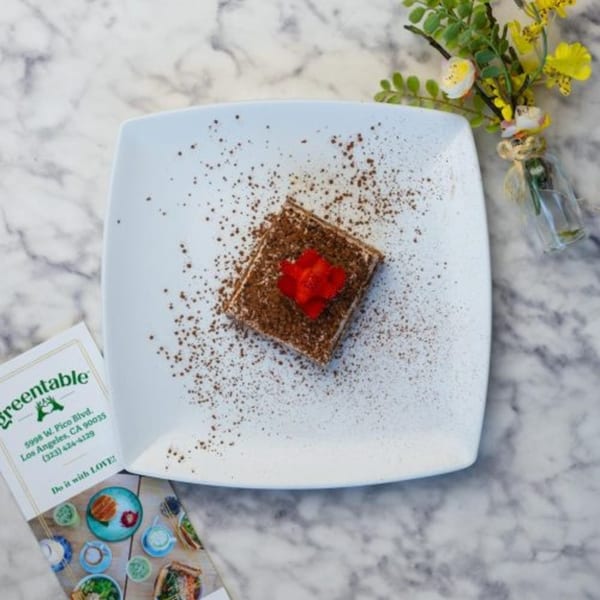 A Green Table Cafe tiramisu dessert with cocoa powder and a red flower on a white plate.