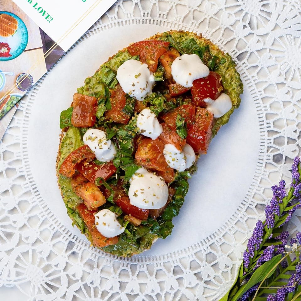 Green Table Cafe's avocado toast with tomatoes, mozzarella, and herbs on a white lace placemat.