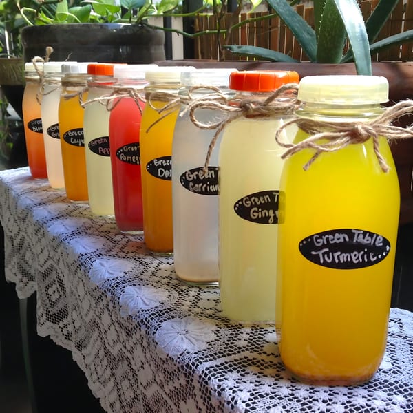 A row of colorful Green Table Cafe bottled juices on a white lace tablecloth.
