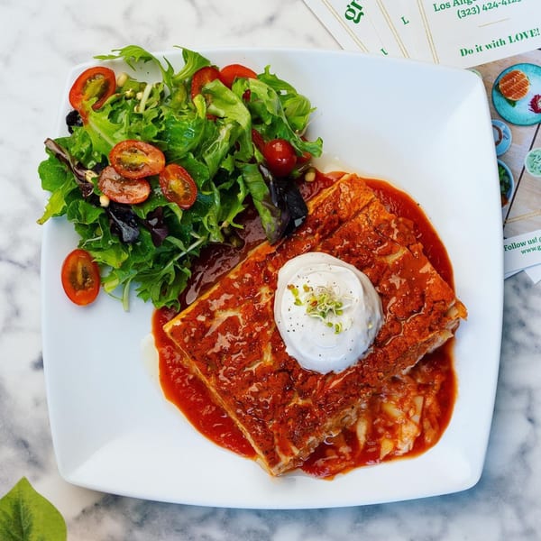 A Green Table Cafe dish featuring a savory pastry in red sauce, topped with cream and sprouts, alongside a fresh green salad.