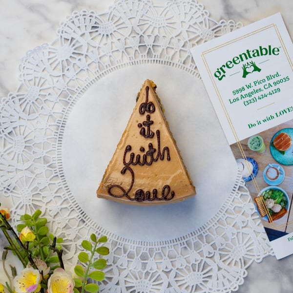 Green Table Cafe's cake slice with "Do it with Love" icing, on a white doily with a menu.
