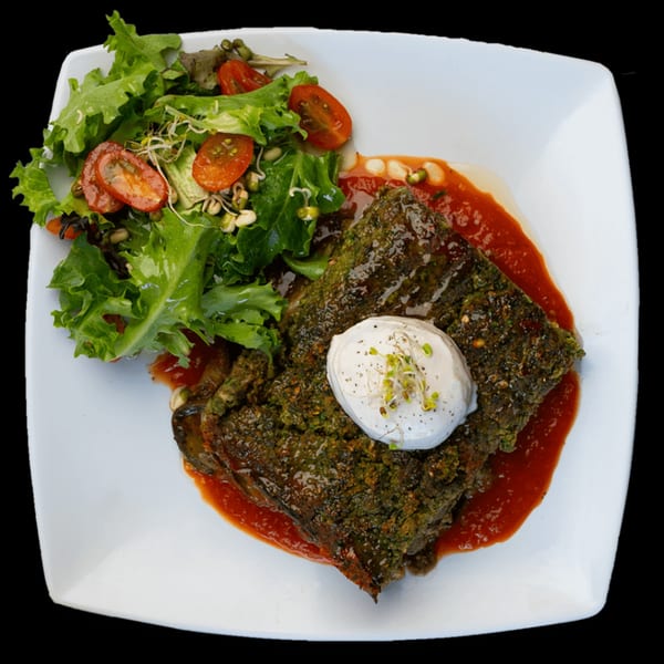 Green Table Cafe's savory green cake with tomato sauce, topped with a dollop of cream and sprouts, served with a side salad.