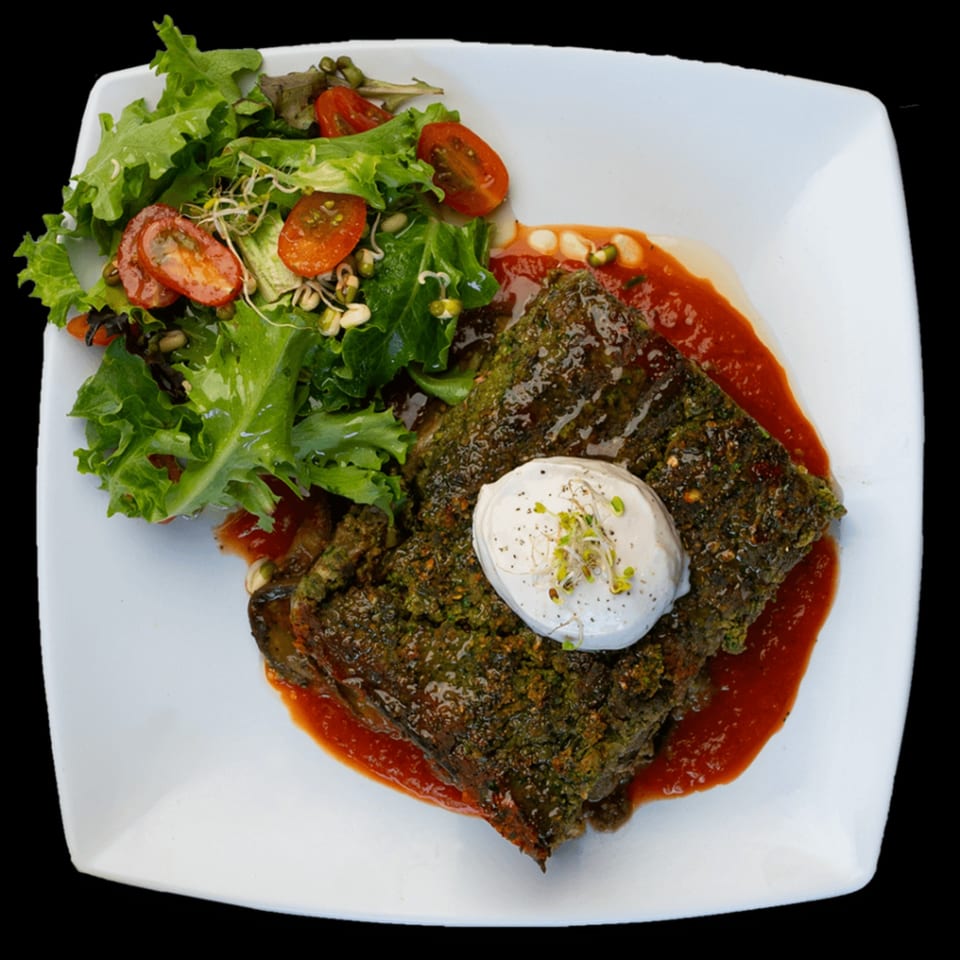 Green Table Cafe's savory green cake with tomato sauce, topped with a dollop of cream and sprouts, served with a side salad.