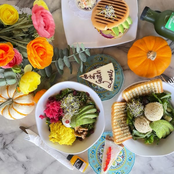 Overhead view of Green Table Cafe's colorful vegan dishes, including salads, a panini, and desserts.