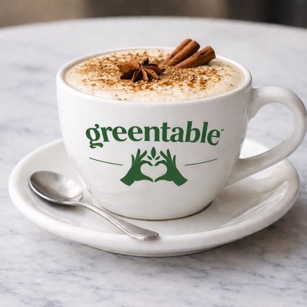 A Green Table Cafe branded mug with a latte, topped with cinnamon, star anise, and cinnamon sticks.
